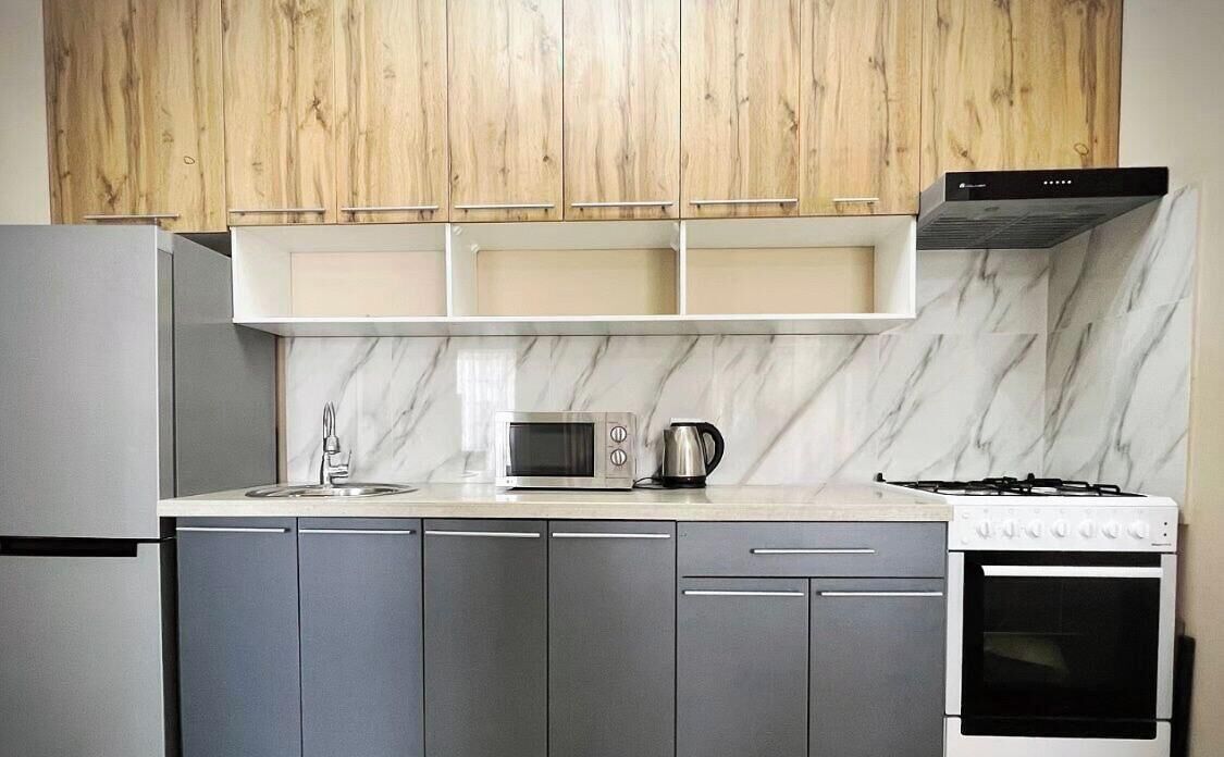 A modern kitchen with grey cabinets, a white countertop, a built-in microwave, a kettle, and a stove.