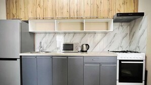 A modern kitchen with grey cabinets, a white countertop, a built-in microwave, a kettle, and a stove. - Apartments Tashkent city Gardens A1 (Tashkent)