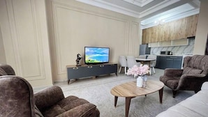 A modern living room with a flat-screen TV, dark sofas, a coffee table, and a kitchen in the background. - Apartments Tashkent city Gardens A1 (Tashkent)