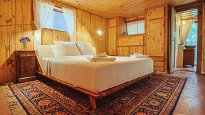 Ein Schlafzimmer einer Holzhütte mit einem Bett, einem Nachttisch, einer Lampe und einem Fenster mit Vorhängen.