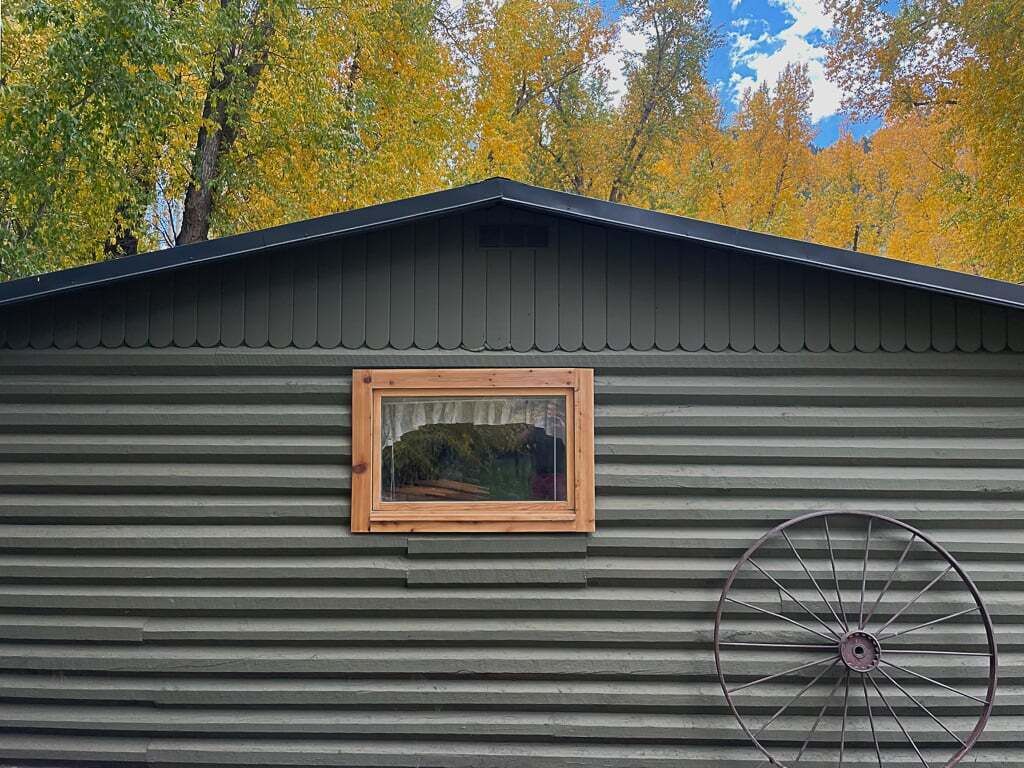 A metal building with a corrugated exterior, a wooden-framed window, and a large wheel-like object attached to the wall.