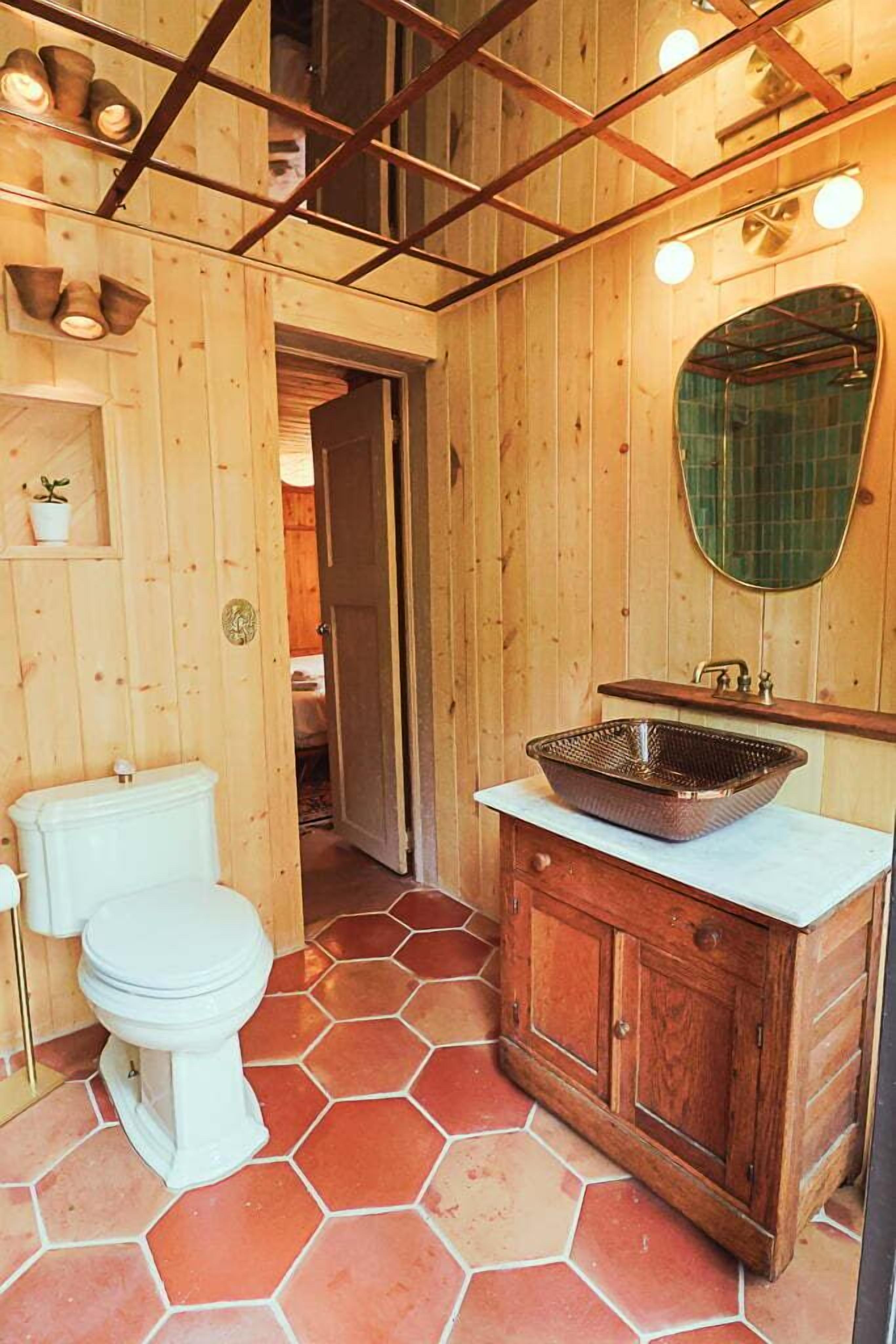 Un baño de madera con inodoro blanco, un mueble de madera con lavamanos y un espejo.