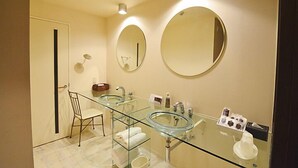 Un baño moderno con dos lavamanos de vidrio, un espejo redondo y una mesita de vidrio con artículos de tocador.