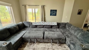 Una sala de estar con un sofá modular, una alfombra y una ventana con cortinas.
