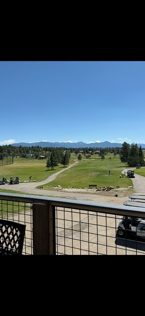 Une vue depuis un balcon donnant sur un terrain de golf, avec un ciel dégagé, des montagnes lointaines et quelques voiturettes de golf.