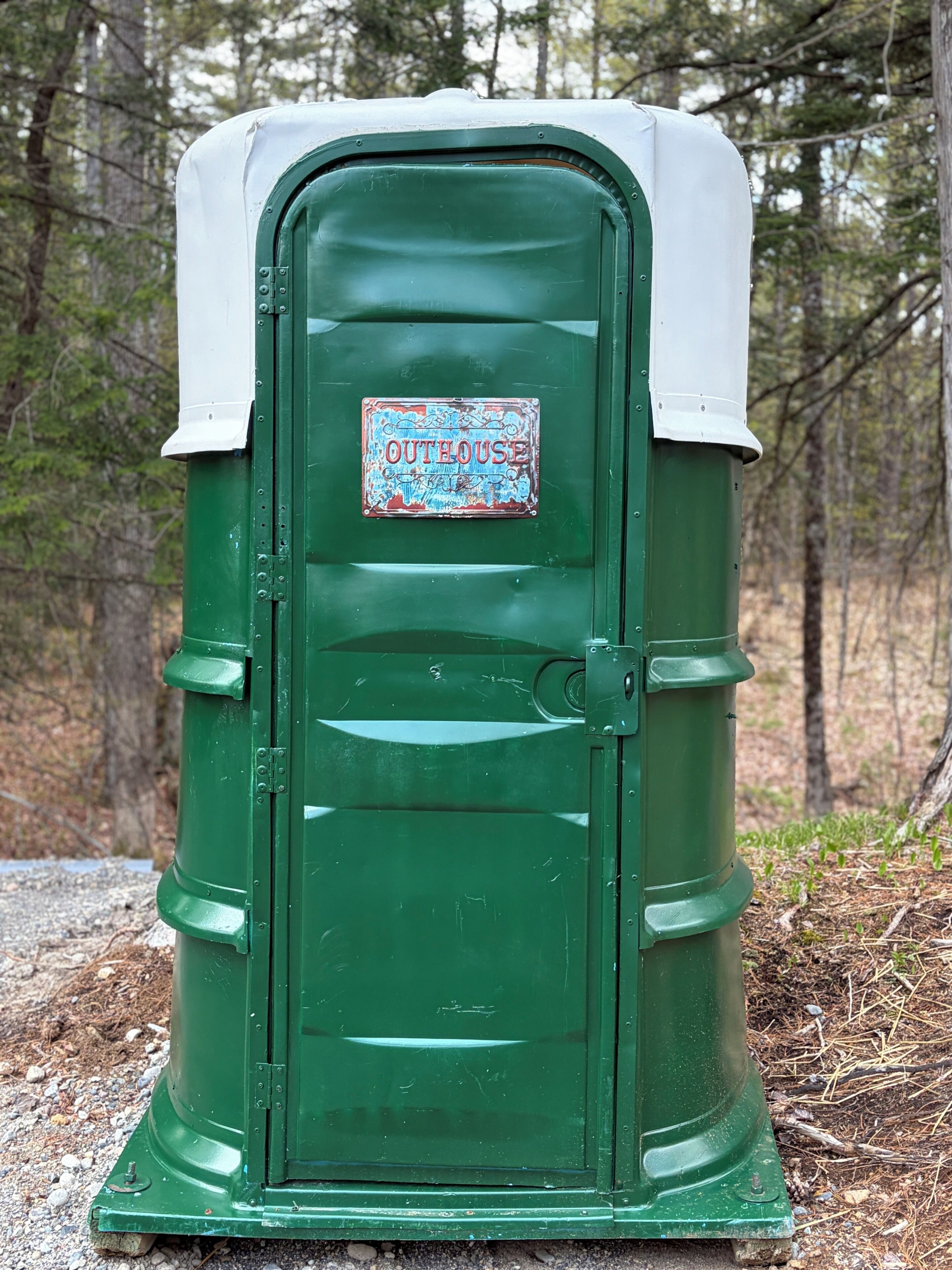 Un petit bâtiment vert servant de toilettes, avec un toit blanc et une pancarte indiquant « TOILETTES ».