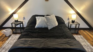 Un dormitorio con una cama negra, almohadas blancas y dos mesitas de noche con lámparas.