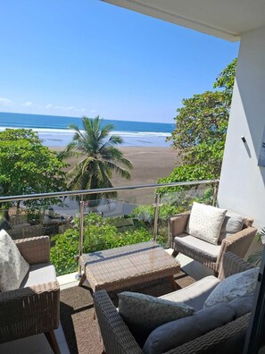 A balcony with wicker furniture overlooking a beach. - Beachfront Ocean View Condo – Family-Friendly with Pools & Wildlife (Esterillos Este)