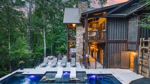 Ein Poolbereich im Freien mit modernem Design, einer Steinstruktur, Liegestühlen und einem Holzgebäude mit Balkon.