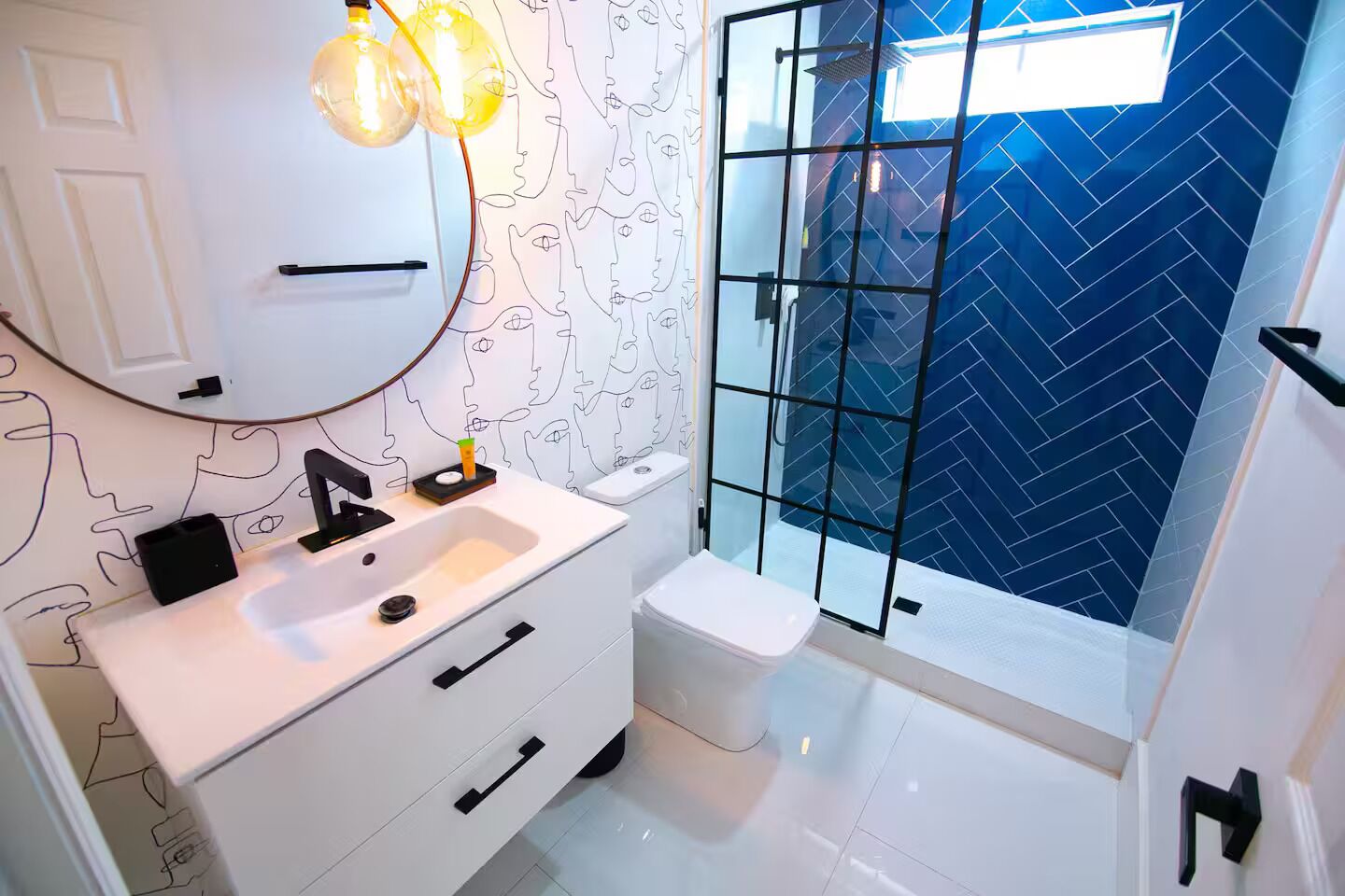 Ein modernes Badezimmer mit einem weißen Waschtisch, einem schwarzen Wasserhahn und einer Duschkabine mit blauer Fischgrätplatten.