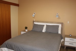 A bedroom with a bed, bedside tables, a nightstand with a plant, and wall-mounted lamps. - Perfect for a retreat or a short stay. Spacious living with clean fresh air. (Willunga)