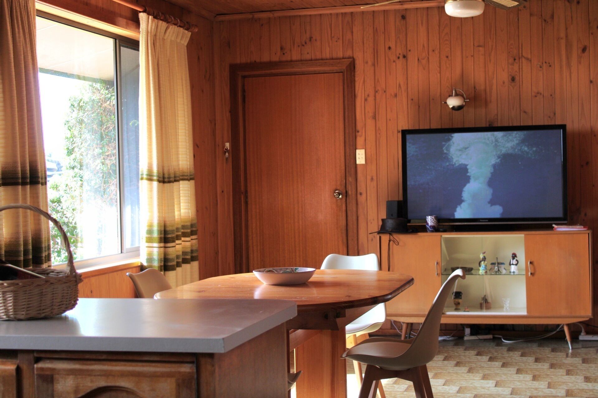 A wooden-paneled room with a dining table, chairs, a television, and a cabinet with glass doors.