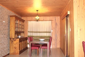 A wooden-paneled room with a dining table, chairs, a chandelier, and a brick wall. - Perfect for a retreat or a short stay. Spacious living with clean fresh air. (Willunga)