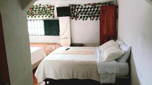 Een slaapkamer met een bed, een televisie, een houten garderobe en een raam met uitzicht.