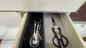 A drawer containing a spoon, a pair of scissors, and a black fabric lining.