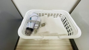 A white plastic laundry basket containing a vacuum cleaner and a white cloth.