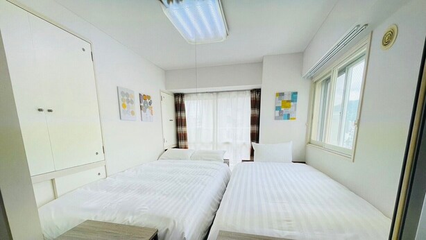 A hotel room with two beds, a small table, and a window with curtains.