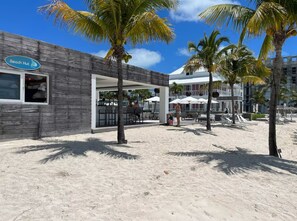 Uma cabana de praia com fachada de madeira, palmeiras e uma área de praia arenosa.