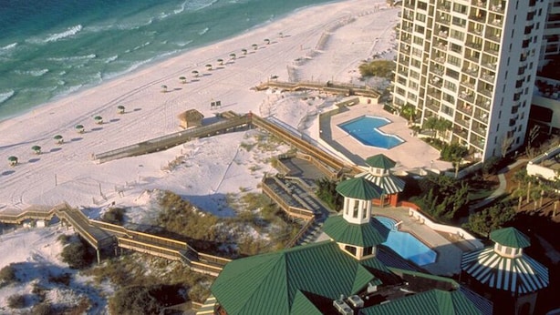 An aerial view of a beach resort with a large hotel, a swimming pool, and a beach area with umbrellas. - 2 Golf Carts ☀️ Screened Patio | Heated Pool | Beach Gear | On Golf Course ☀️ Sandestin (Miramar Beach)