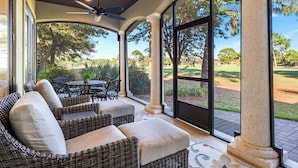 A covered patio with wicker furniture and large windows overlooking a golf course. - 2 Golf Carts ☀️ Screened Patio | Heated Pool | Beach Gear | On Golf Course ☀️ Sandestin (Miramar Beach)