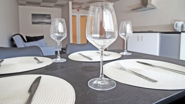 A dining table set with white plates, cutlery, and three clear wine glasses.