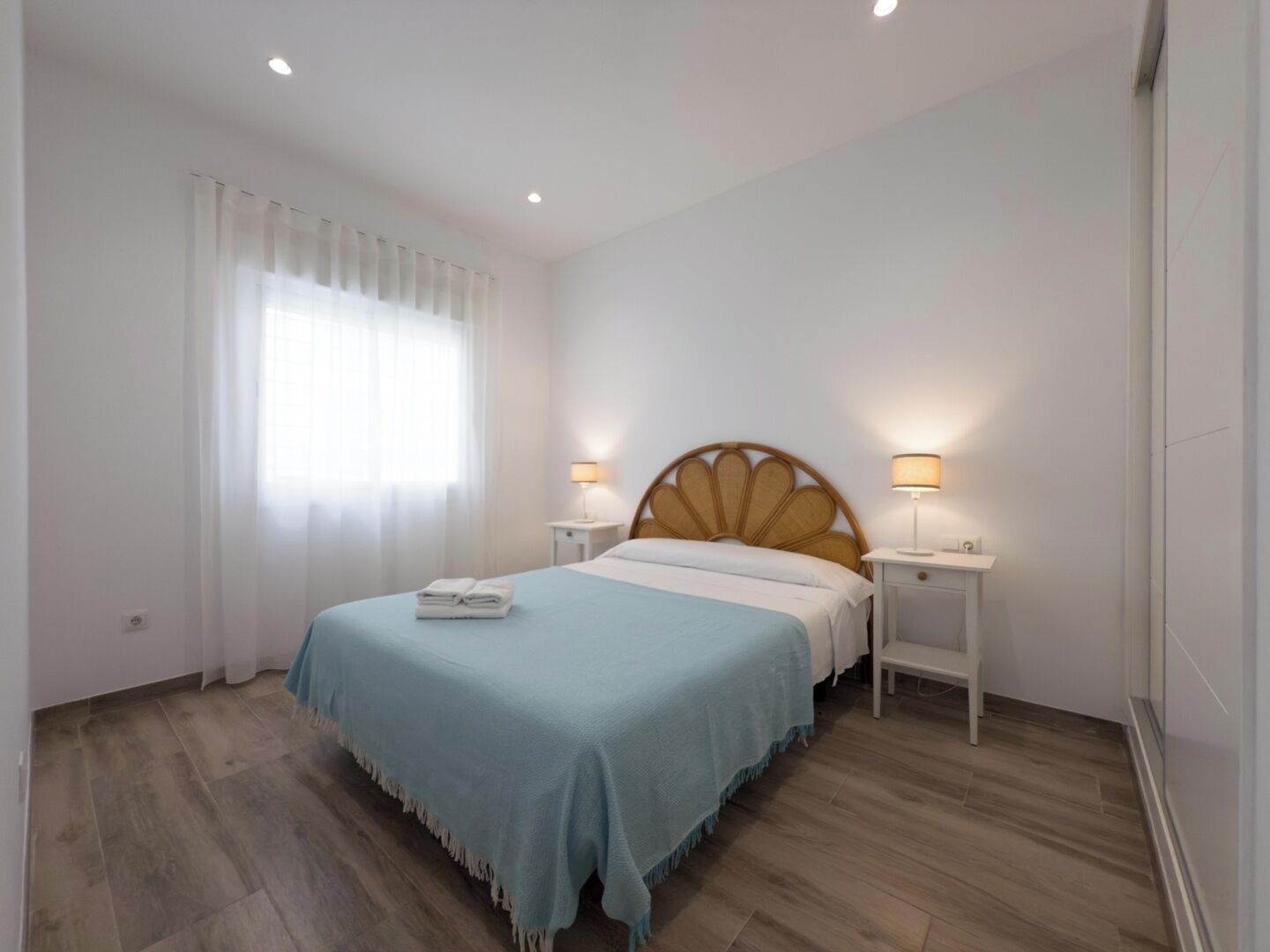 Een hotelkamer met een bed, twee nachtkastjes, een raam met gordijnen en een houten vloer.