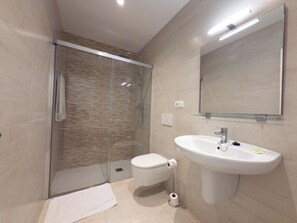 Un baño moderno con cabina de ducha de vidrio, inodoro blanco y lavamanos sobre pedestal.