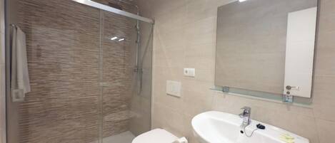 A modern bathroom with a glass shower enclosure, a toilet, and a sink with a mirror above it.