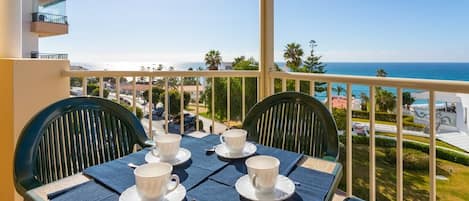 A balcony with a table set for two, overlooking a coastal view.