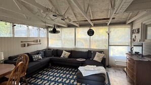 Una sala de estar acogedora con un sofá modular oscuro, una mesa de comedor de madera con sillas y un tapete estampado.