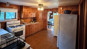 Una cocina con paredes de madera, estufa, refrigerador y ventilador de techo.