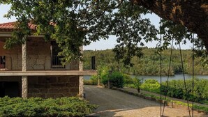 Ein Steinhäuschen mit Balkon, das auf einen See mit viel Grün und einer Schaukel blickt.