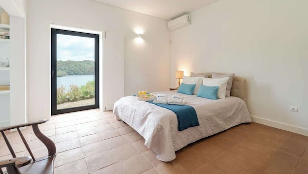 Ein Schlafzimmer mit einem Bett, einem Nachttisch, einer Lampe und Seeblick durch eine Schiebetür.