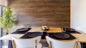 Una mesa de comedor con cuatro sillas, manteles individuales negros y un bol de fruta.