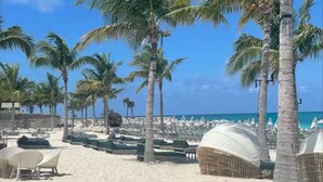 Ein Strand mit Palmen, Liegestühlen und Sonnenschirmen.