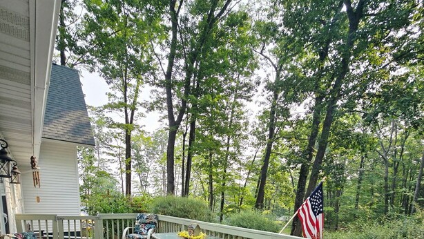 A wooden deck with outdoor furniture, a table, and an American flag. - Quiet Higgins Lake home close to ATV trail, Boat Launch, and Silver Dollar! (Roscommon)