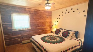 A cozy room with a wooden ceiling, a bed with a quilt, a window with curtains, and a wall with paw prints. - Quiet Higgins Lake home close to ATV trail, Boat Launch, and Silver Dollar! (Roscommon)