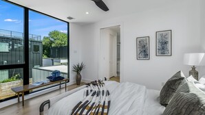 A modern bedroom with a large window, a ceiling fan, and two framed artworks. - Stunning Modern Zilker Home with Private Pool, Designer Touches & Prime Location (Austin)