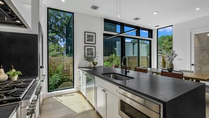 A modern kitchen with a large island, stainless steel appliances, and large windows offering a view of the outdoors. - Stunning Modern Zilker Home with Private Pool, Designer Touches & Prime Location (Austin)