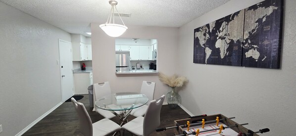 A dining area with a glass table, white chairs, and a world map on the wall.