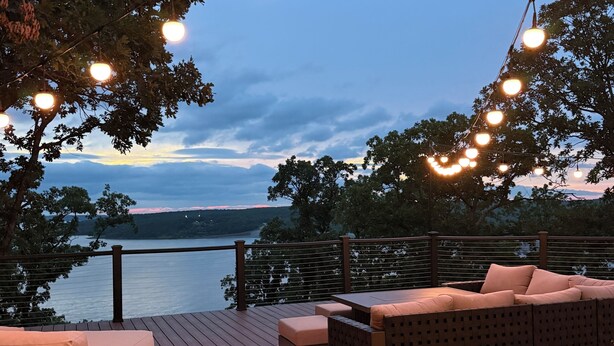 Terraza con sofá y cojines, luces colgantes y vista a un cuerpo de agua.