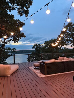 Terraza con sofá y cojines, luces colgantes y vista a un cuerpo de agua.