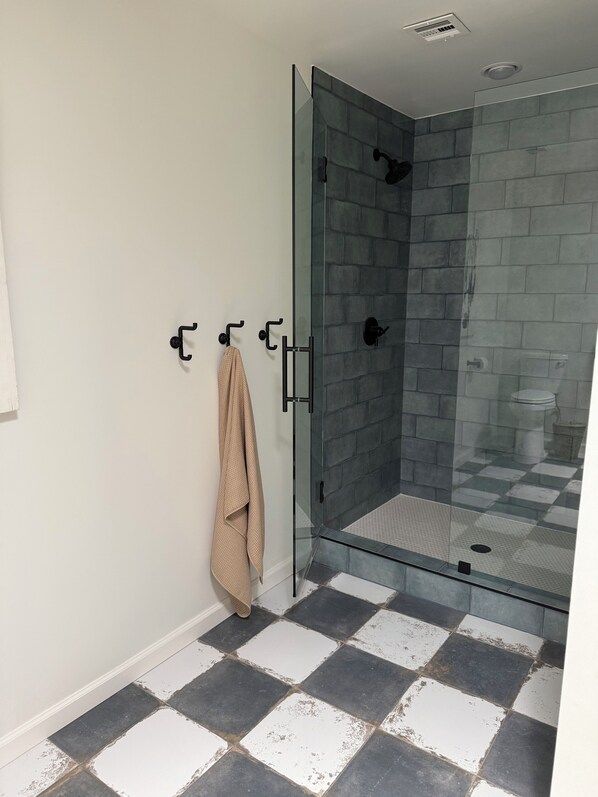 Un baño con cabina de ducha de vidrio, un perchero y un suelo a cuadros.