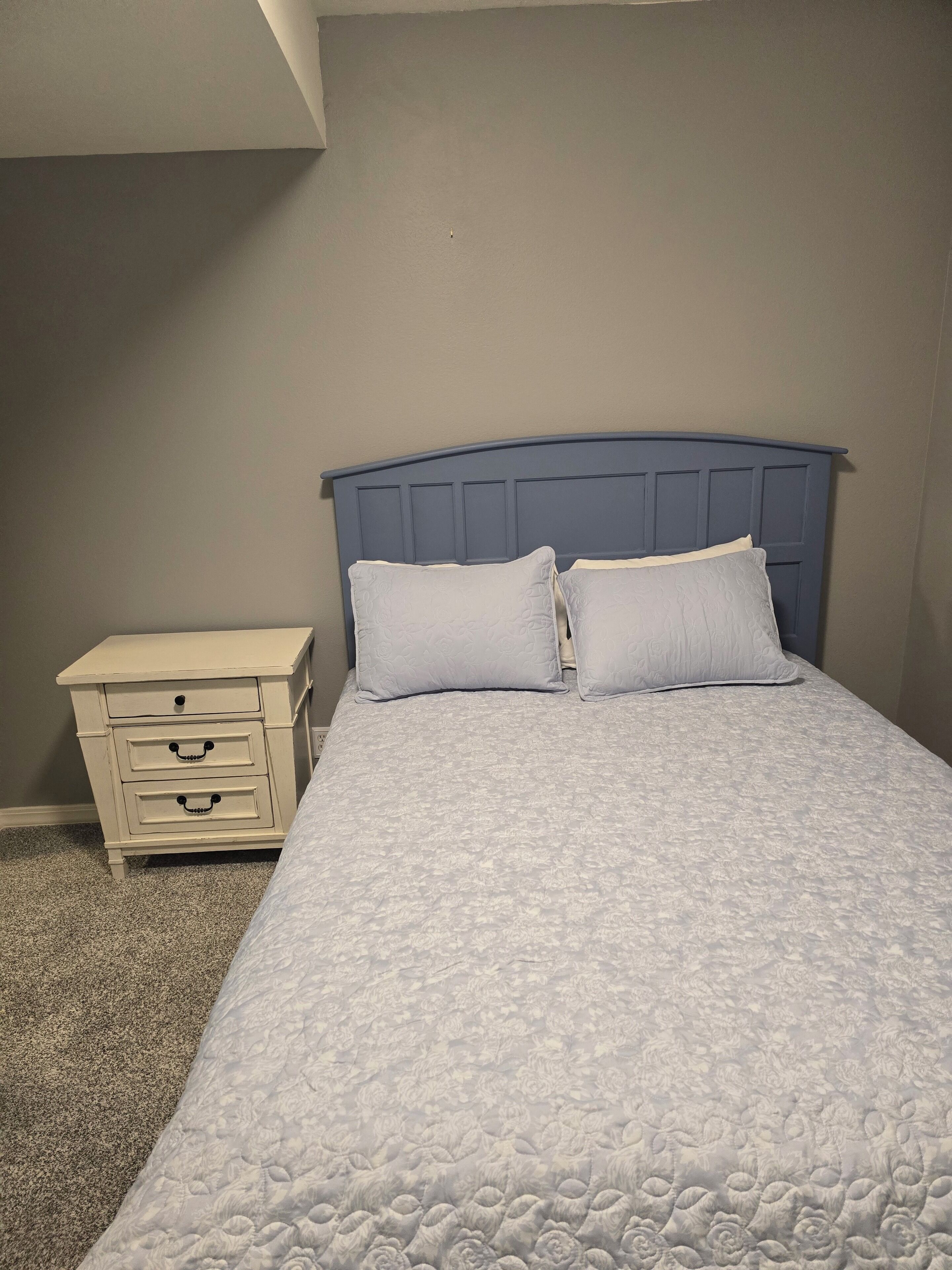 Une chambre à coucher avec un lit, deux oreillers et une table de chevet dotée de tiroirs.