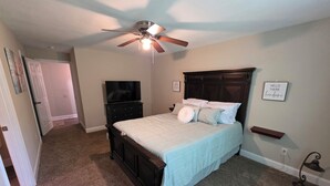 A bedroom with a bed, a ceiling fan, a TV, and a bedside table.