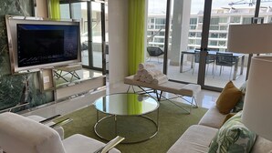 Ein modernes Hotelzimmer mit Flachbildfernseher, einem Glastisch, einer Couch und einer Bank mit Handtüchern.