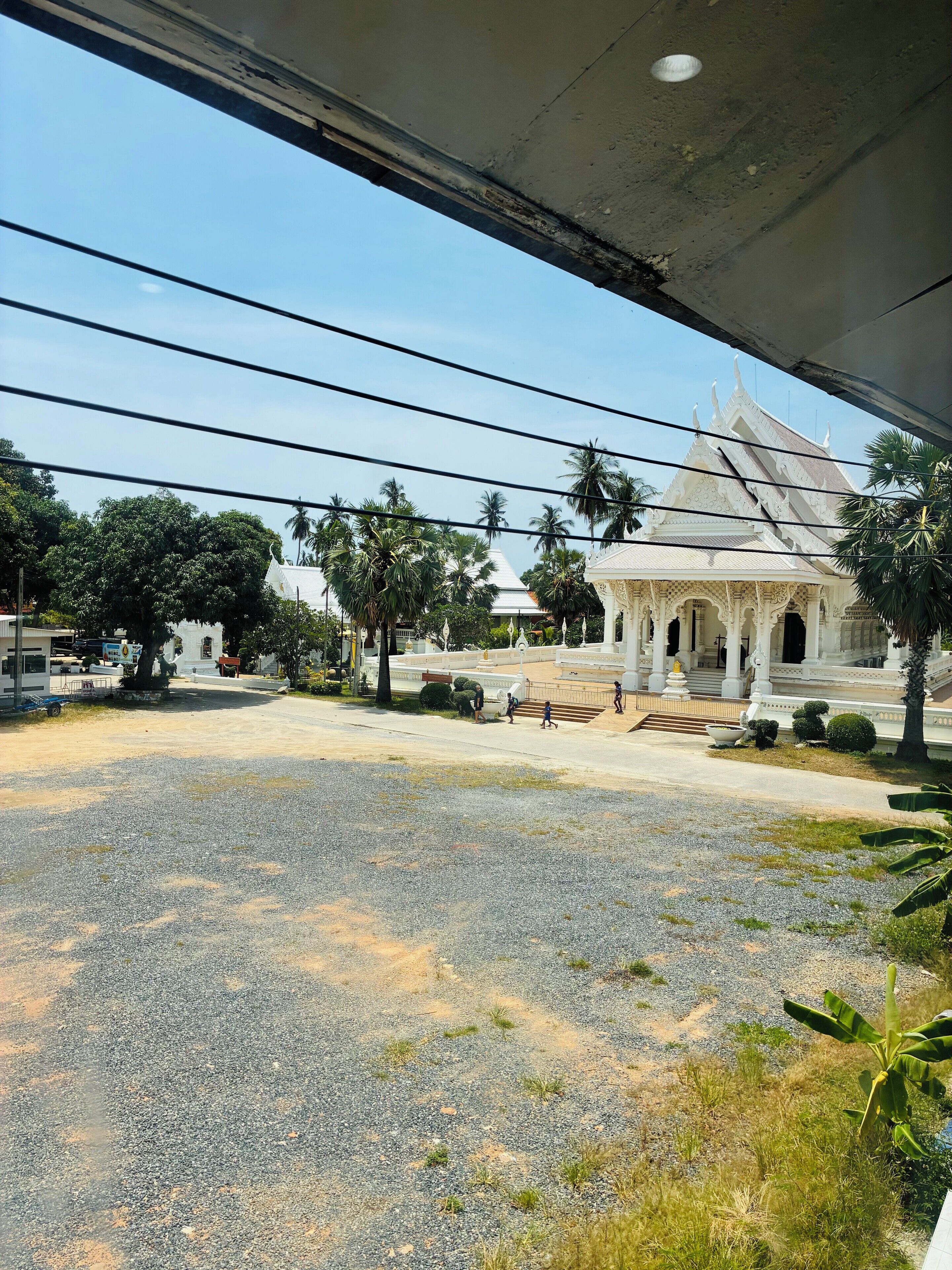 Vista de un templo de estilo arquitectónico tradicional, rodeado de palmeras y un patio de grava.
