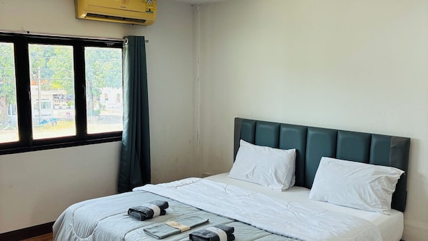 A hotel room with a bed, wooden flooring, a window with curtains, and an air conditioning unit. - Apartment Wat Sawang Arom 08 (Koh Samui)