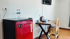 A compact kitchenette with a red refrigerator, a wooden dining table, and a TV mounted on the wall. - Apartment Wat Sawang Arom 08 (Koh Samui)