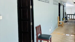 A hallway with a wooden door, a chair, and a mat with a cartoon character. - Apartment Wat Sawang Arom 08 (Koh Samui)